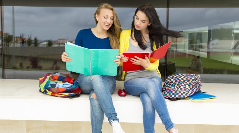 Estudantes sentadas lendo cadernos coloridos.